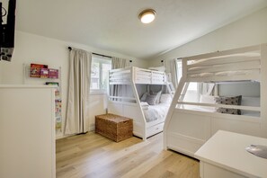 A bunk bed room with a desk, a basket, and a window with curtains.