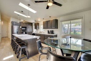A modern kitchen with a central island, bar stools, a glass dining table, and a ceiling fan.