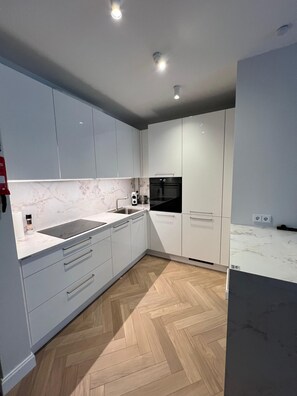 A modern kitchen with white cabinets, a black oven, and a marble countertop. - Kalpaka Residence Apartment  (Rīga)