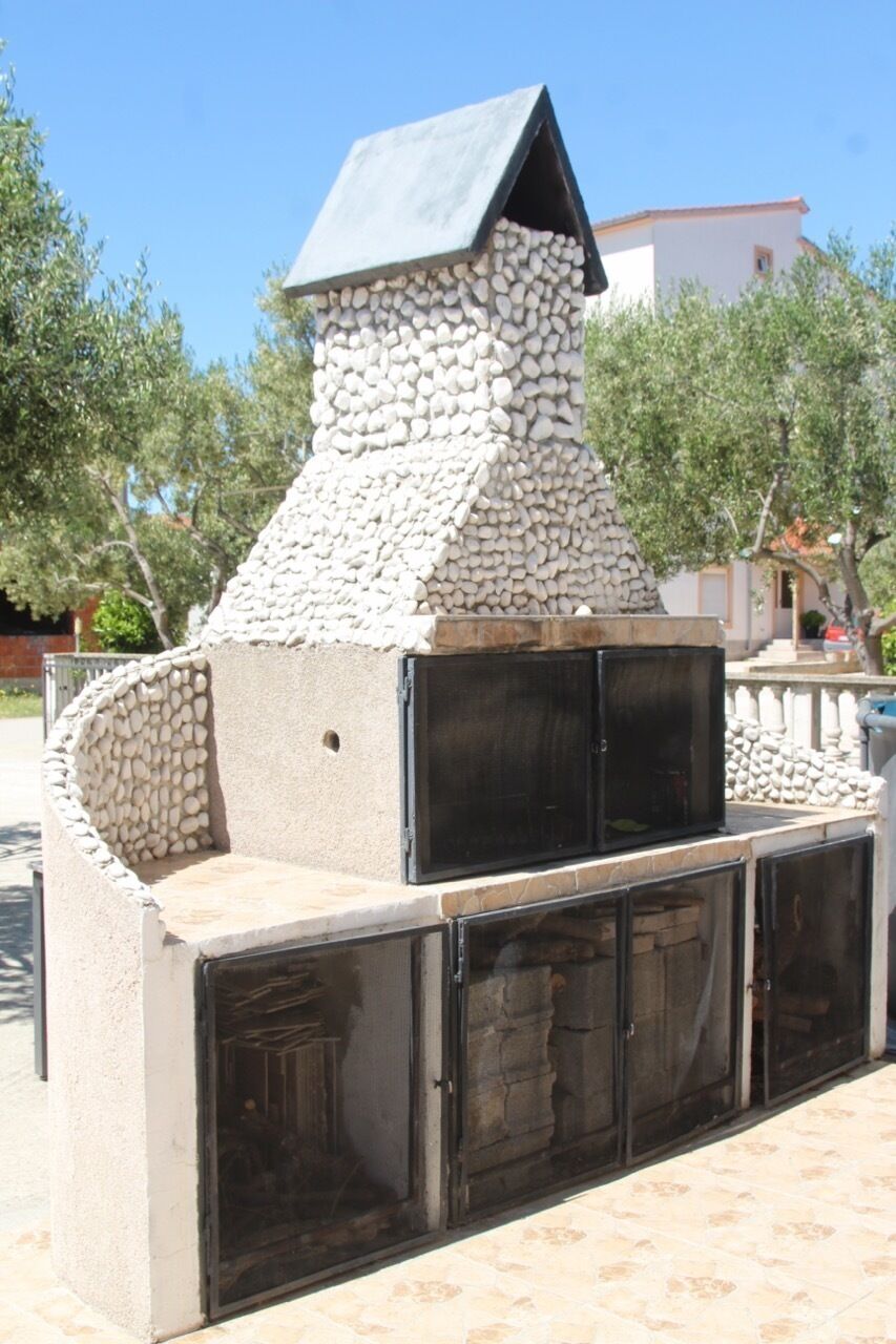 Cocina al aire libre de piedra con chimenea, una parrilla y un espacio para sentarse.