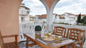 A balcony with a wooden table and chairs, a potted plant, and a bottle of wine. - Spacious Apartment with Large Balcony, Parking & Walk to Beach (Vodice)