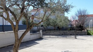 Ein Parkplatz mit Baum, Metalltor und einem Gebäude im Hintergrund.