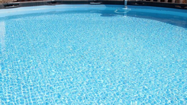 Ein klares, blaues Schwimmbecken mit einer gefliesten Kante und einem sichtbaren Wasserspiel.