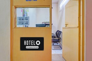 Een hotel receptie met een bord waarop de inchecktijd staat, een receptiebalie en een zithoek met stoelen.