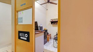 A reception area with a sign indicating 'RECEPTION' and a booking time sign. There is a desk with a computer and a chair. - Hotel O Delmon Residency (Chennai)