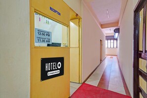 Een hotel receptie met een receptiebalie, een bord met openingstijden voor reserveringen en uitchecken, en een bord voor het hotel 'HOTELO'.