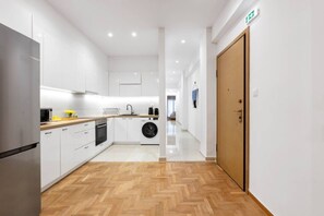 Eine moderne Küche mit weißen Schränken, einer Holzarbeitsplatte, einer Waschmaschine und einer Holztür.
