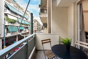 Ein Balkon mit Tisch und Stuhl, einem Blumentopf und Blick auf benachbarte Gebäude.
