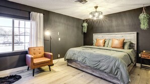 Ein Schlafzimmer mit einem Bett, einem Stuhl, einem Fenster und einer hängenden Pflanze.