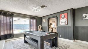 Ein Billardtisch in einem Raum mit Blick nach draußen, eine Uhr an der Wand und ein gerahmtes Bild.