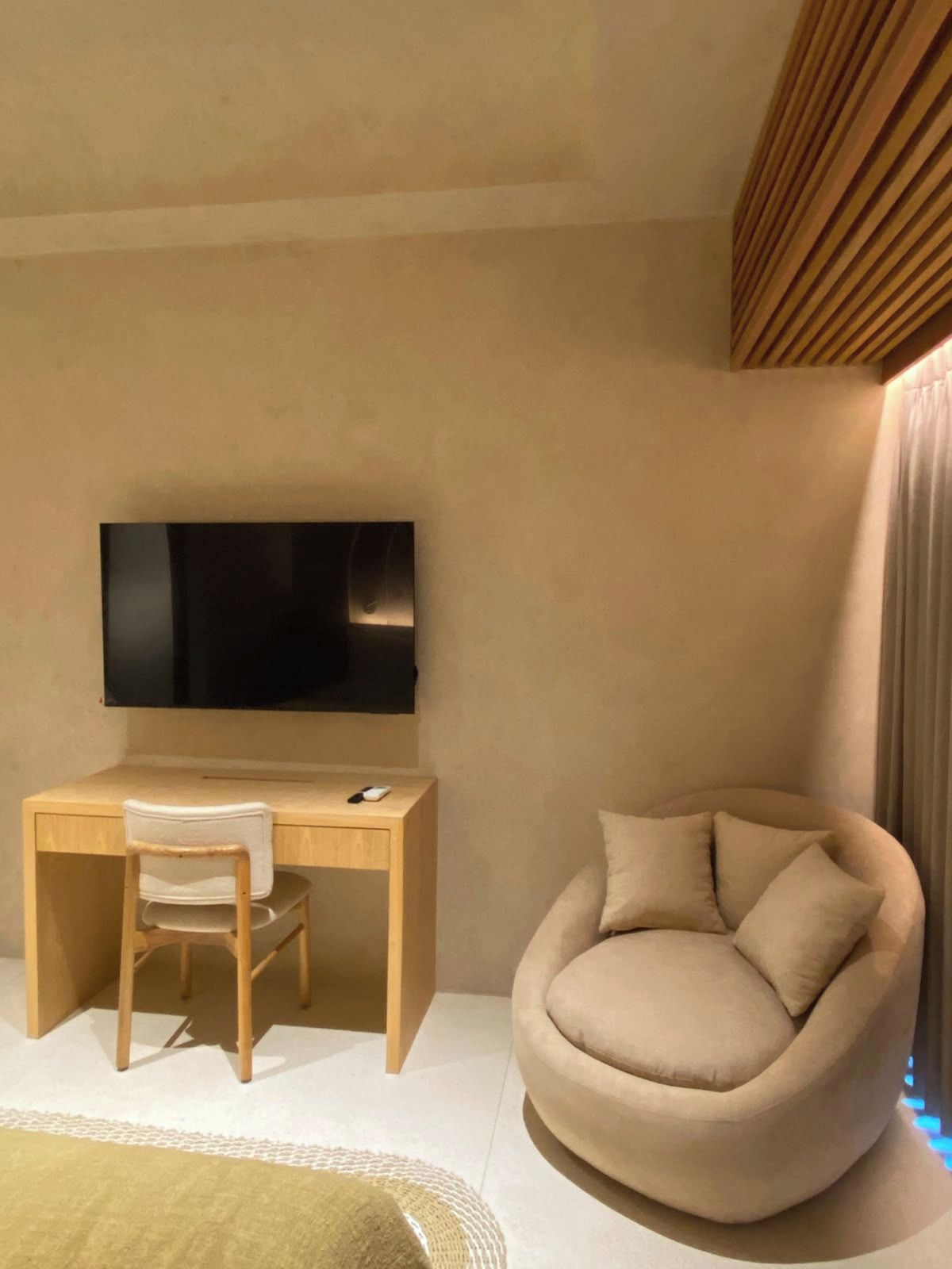 Een moderne kamer met een flatscreen televisie aan de muur, een houten bureau met stoel, en een ronde, comfortabele zithoek.