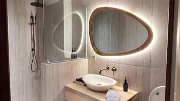 Un baño moderno con tocador de madera, un espejo redondo, ducha y un inodoro.