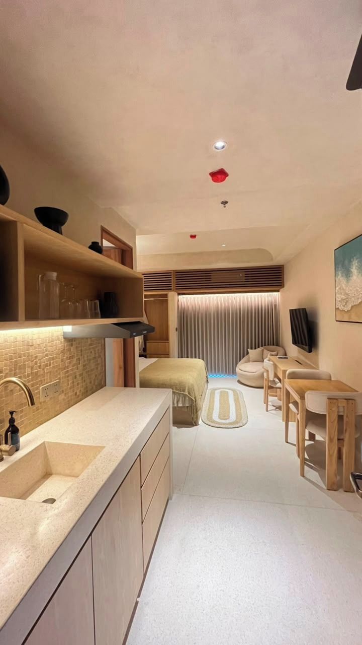 Un espacio habitable compacto con kitchenette, zona de estar y televisor montado en la pared.