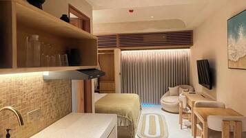 Un espacio habitable compacto con kitchenette, zona de estar y televisor montado en la pared.