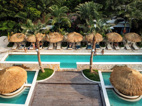 A pool area with lounge chairs and thatched umbrellas, surrounded by palm trees.