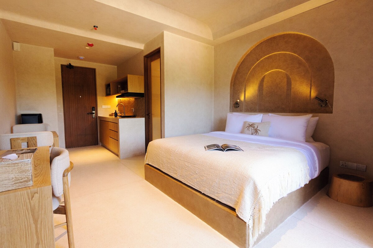 Habitación de hotel con cama, escritorio, silla, kitchenette pequeña y baño.