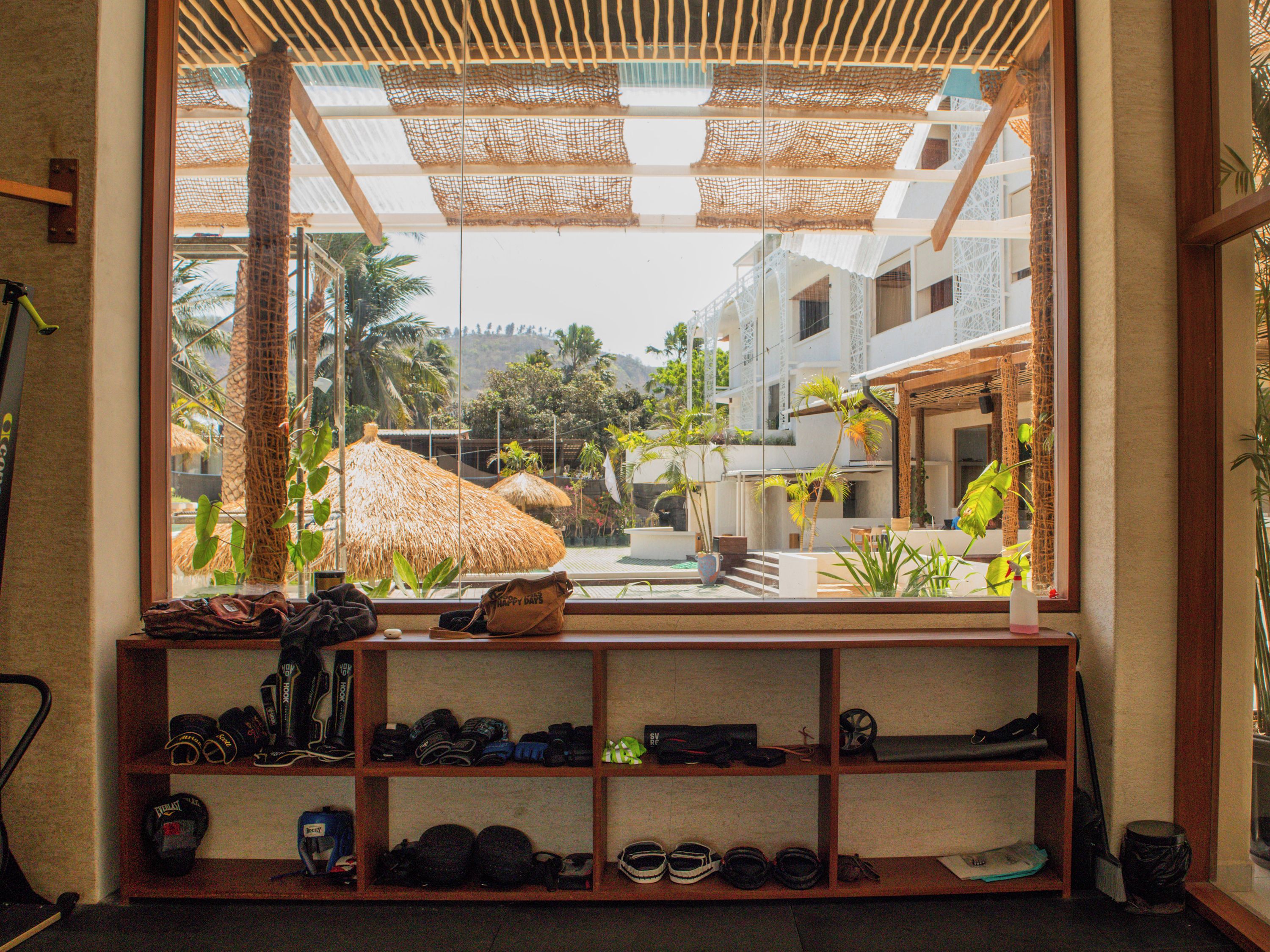 A room with a view of a tropical resort, a shelf with various items, and a window with a view of palm trees and buildings.