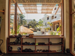 A room with a view of a tropical resort, a shelf with various items, and a window with a view of palm trees and buildings.