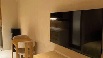 Una habitación moderna con un escritorio de madera, una silla, un televisor fijado a la pared y una mesita con un control remoto.