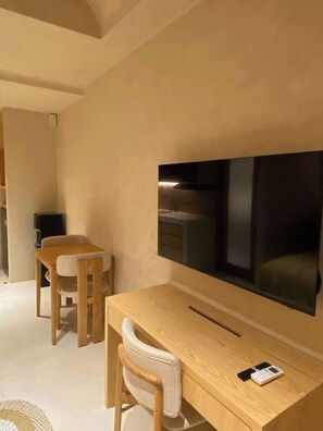 A modern room with a wooden desk, a chair, a television mounted on the wall, and a small table with a remote control.