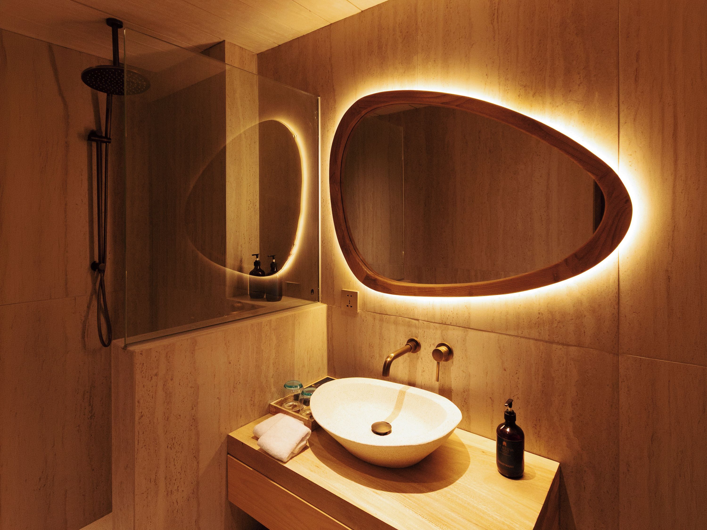 A modern bathroom with a large oval mirror, a round sink, and a handheld showerhead.