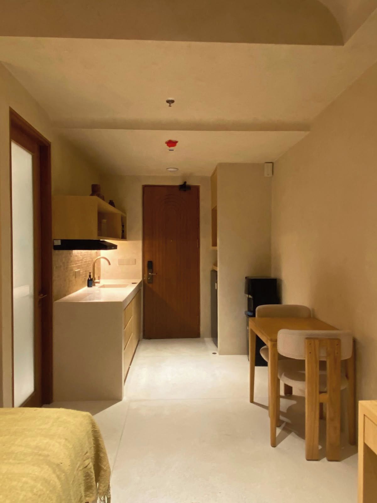 A narrow hallway with a wooden door at the end, a small sink, and a table with a chair.