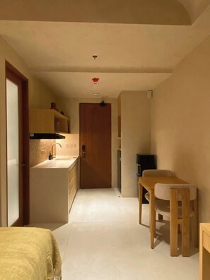 Un pasillo estrecho con una puerta de madera al final, un lavamanos pequeño y una mesa con una silla.