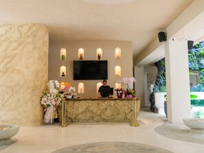 A reception desk with a flat-screen TV, multiple wall-mounted lights, and a stone wall backdrop.