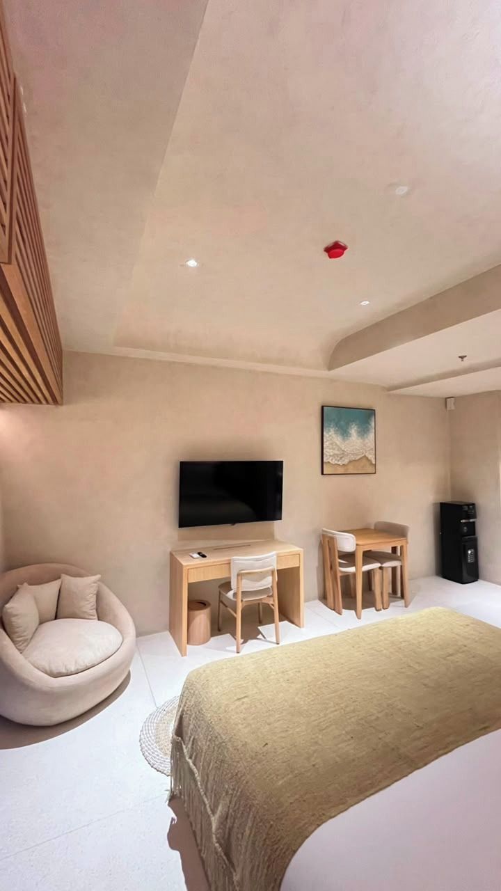 Un dormitorio moderno con cama, escritorio, silla, televisor y un cuadro en la pared.