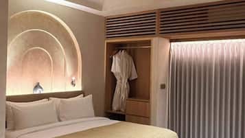 A modern hotel room with a large bed, a wooden side table, a wardrobe, and a window with curtains.