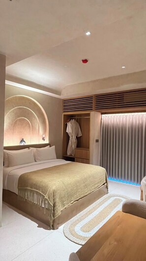 A modern hotel room with a large bed, a wooden side table, a wardrobe, and a window with curtains. - Atrium Lombok (Lombok)