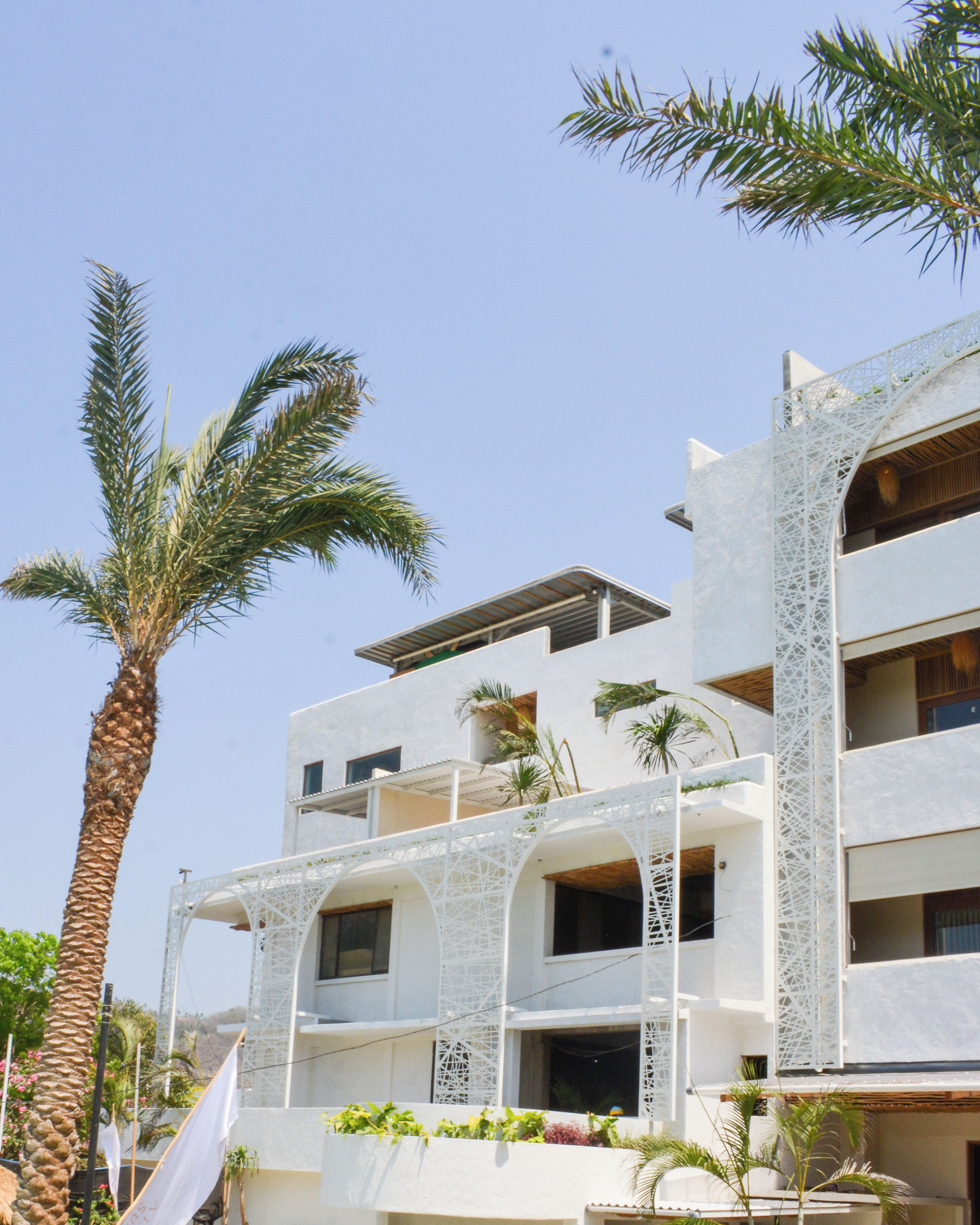 Un edificio de varios pisos con balcones, palmeras y un cielo despejado.