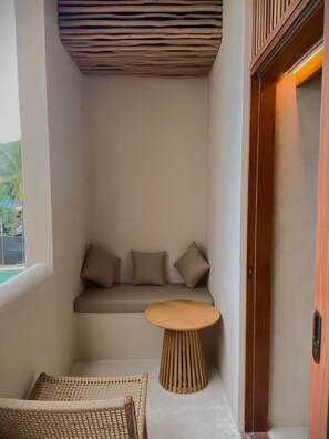 A corner room with a built-in bench, a small round table, and a wicker chair. - Atrium Lombok (Lombok)