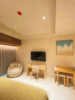A modern bedroom with a bed, a desk, a chair, a television, and a painting on the wall.