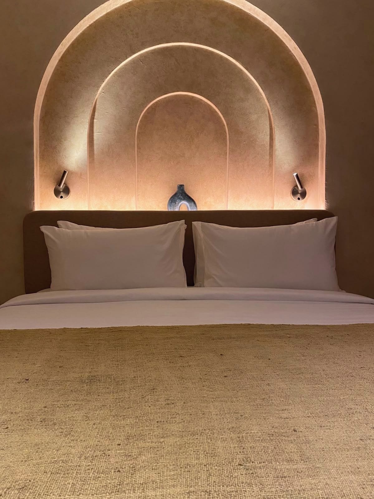 A bed with a headboard featuring an arched design and two wall-mounted light fixtures.
