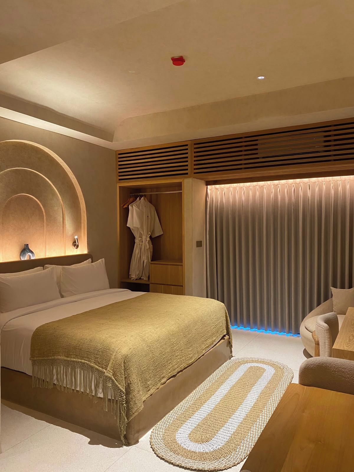 Habitación de hotel moderna con una cama grande, zona de estar, armario y ventana con cortinas.