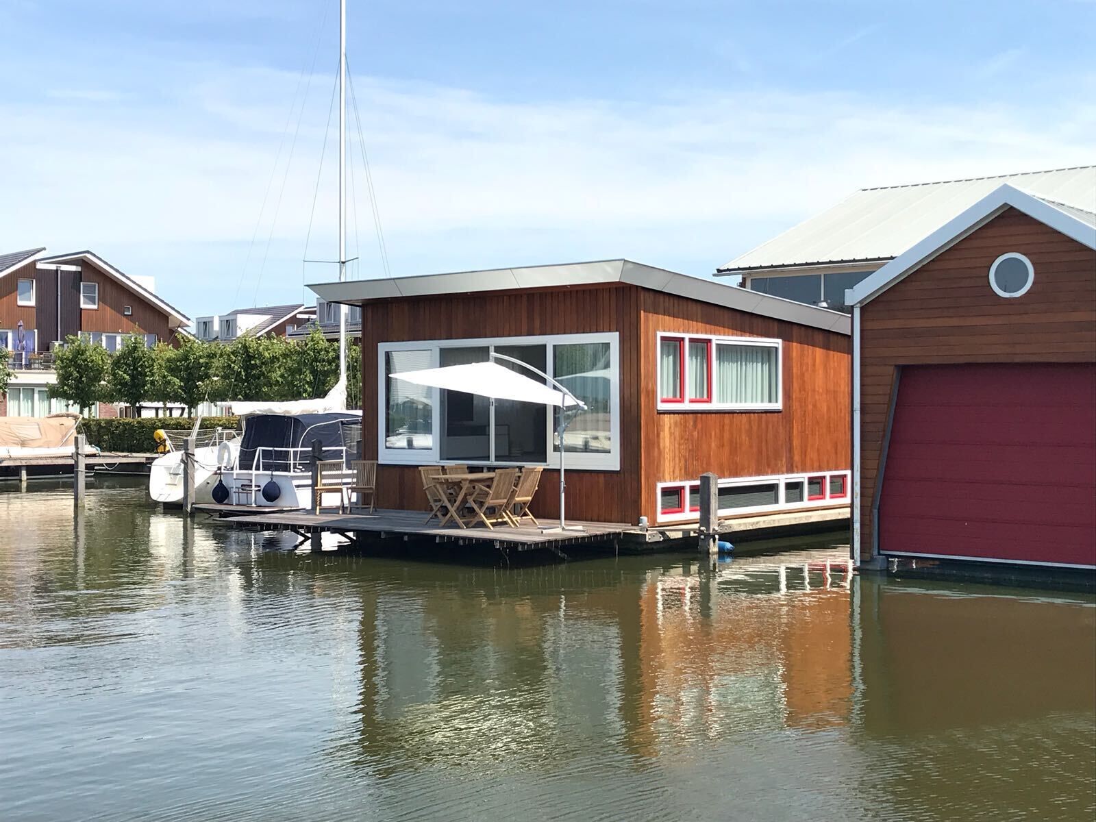 Een moderne rijkszacht met een groot raam, een klein dek met een tafel en stoelen, en een rode garage.