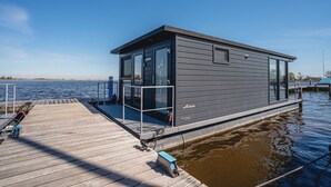 Una moderna casa galleggiante con un pontile, ampie finestre e vista libera sull'acqua.