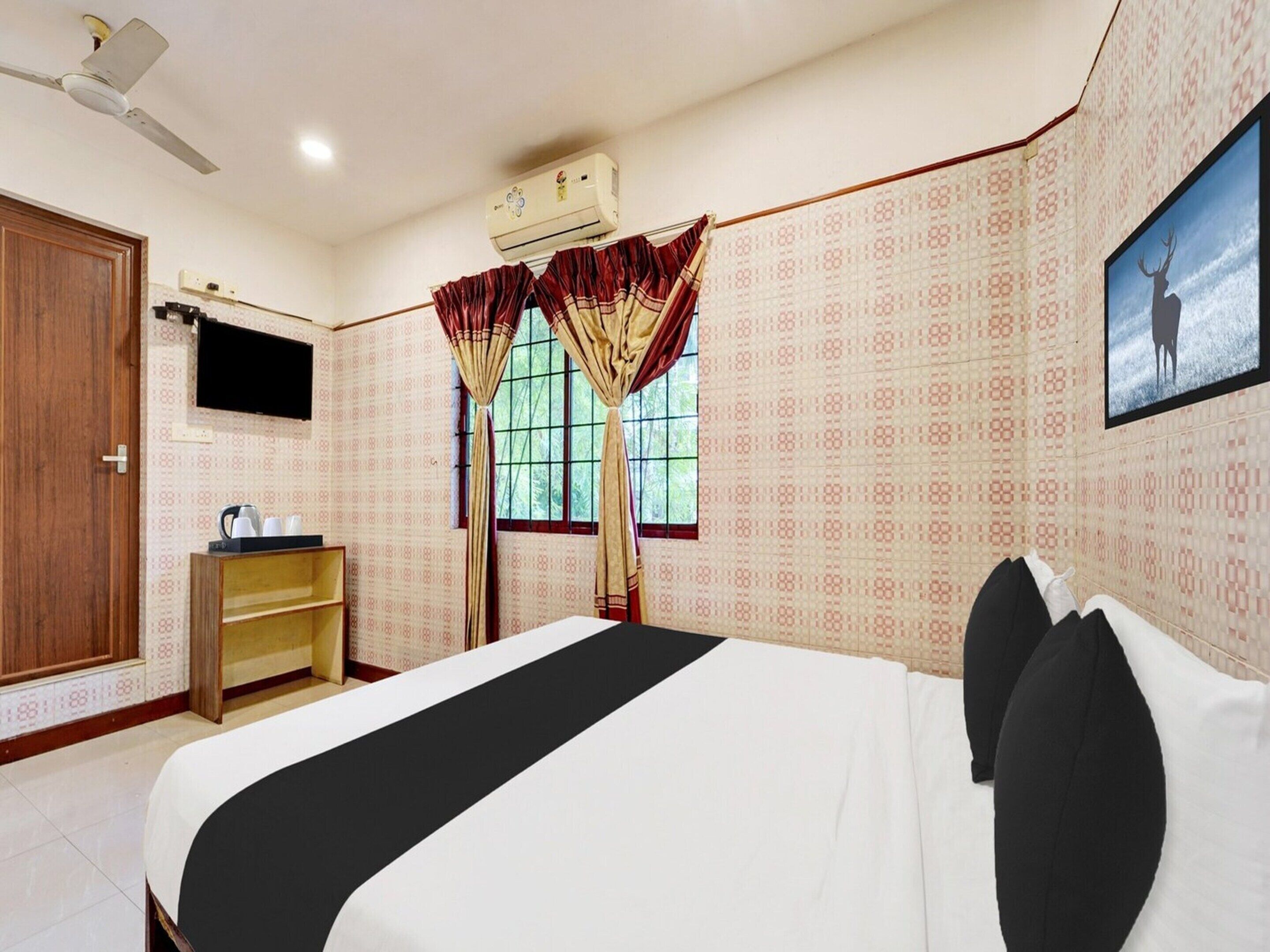 A hotel room with a bed, a TV, an air conditioner, a wooden cabinet, and patterned wallpaper.
