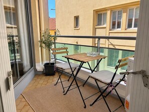 Ein Balkon mit Tisch und Stühlen, einem Blumentopf und Blick auf benachbarte Gebäude.