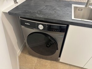 A compact washer and dryer unit with a control panel, located in a small kitchen area with a countertop and a sink. - L'écrin Sétois - T2 Air-conditioned - Walking distance to train station and center of Sète (Sète)