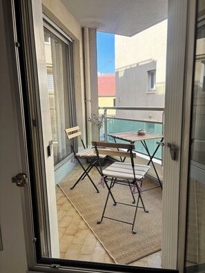 A balcony with a table and chairs, a view of buildings, and a door leading to the interior. - L'écrin Sétois - T2 Air-conditioned - Walking distance to train station and center of Sète (Sète)