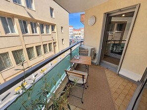 A balcony with a view of the street, a table, chairs, and a potted plant. - L'écrin Sétois - T2 Air-conditioned - Walking distance to train station and center of Sète (Sète)