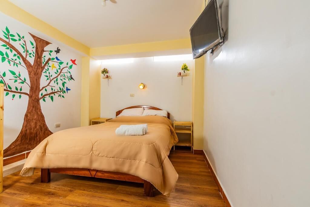 Ein Schlafzimmer mit einem Bett, einem an der Wand befestigten Fernseher und einer Baummalerei.