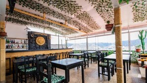 A restaurant with a bar, tables, chairs, and a view of mountains. - Sueños de San Blas Hostel (Cusco)