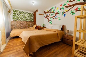 Una habitación con dos camas, piso de madera, pared de piedra, mesita de noche de madera y un mural en la pared.