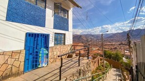 A building with a blue door and windows, a stone wall, and a view of a valley with mountains in the background. - Sueños de San Blas Hostel (Cusco)