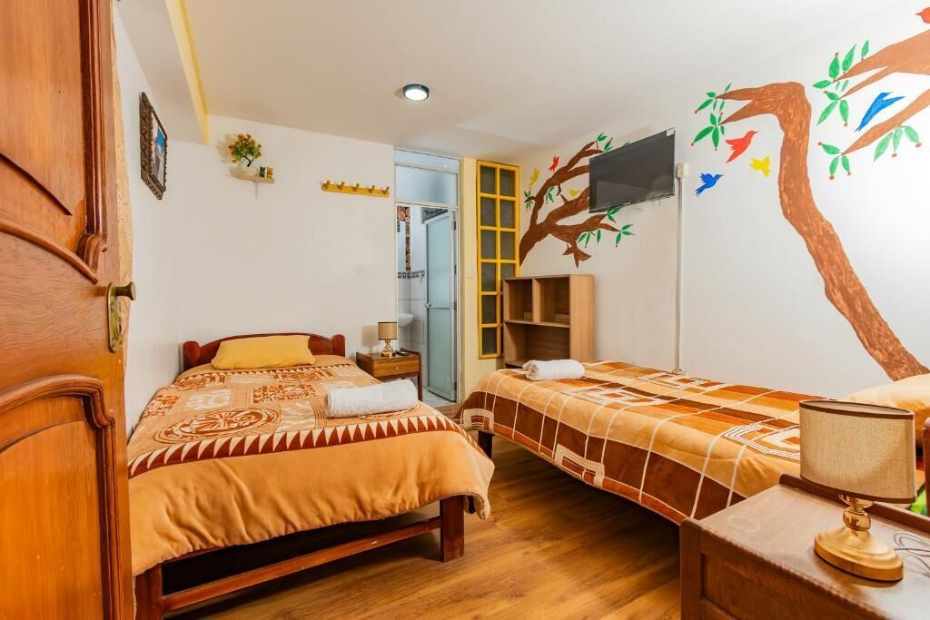 Camera da letto con due letti, una TV, un'armadio in legno e un affresco raffigurante un albero.