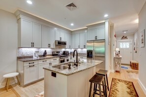 Eine moderne Küche mit weißen Schränken, Granit Arbeitsplatten, einer zentralen Kochinsel mit Hockern und Edelstahlgeräten.