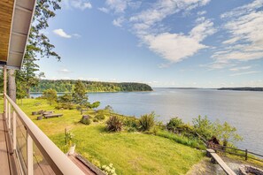 Udsigt over søen fra en balkon med træterrasse, picnicbord og stenvæg.